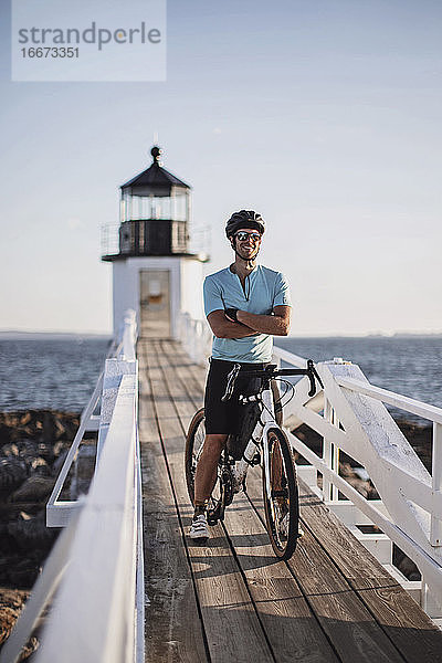 männlicher Radfahrer posiert mit Fahrrad vor einem Leuchtturm an der Küste von Maine