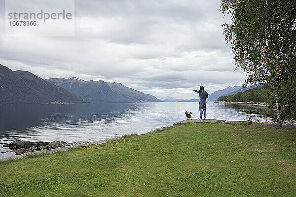 Ein Mann und sein kleiner Hund schauen über einen Fjord in Norwegen