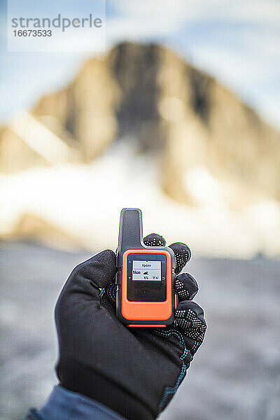 Mountaineer hält Mini-GPS-Gerät mit Wettervorhersage in der Hand.