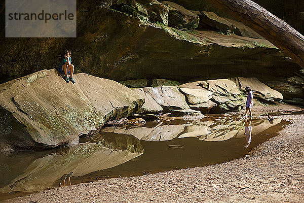 Zwei Kinder spielen ruhig in einer Sandsteinschlucht an einem spiegelnden Becken