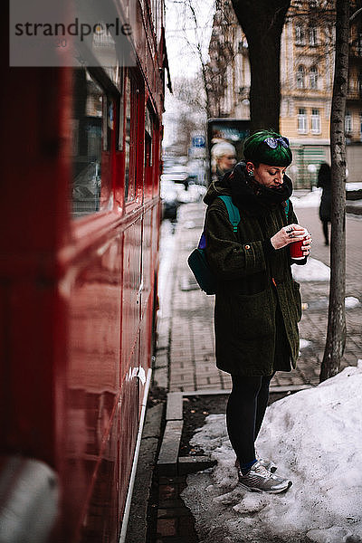 Porträt einer nicht-binären Hipster-Frau  die an einem roten Bus in der Stadt steht