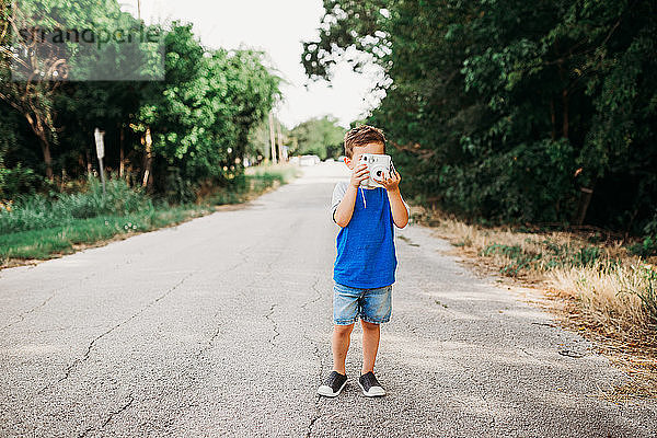 Junge steht draußen und macht ein Foto mit einer Sofortbildkamera