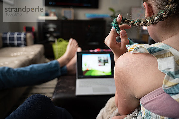 Tween Girl spielt mit Haaren und schaut auf den Laptop im Wohnzimmer