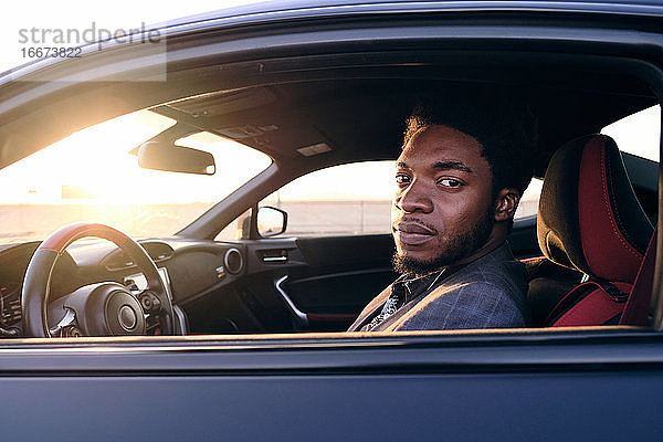 Afroamerikanischer Geschäftsmann im Sportwagen bei Sonnenuntergang