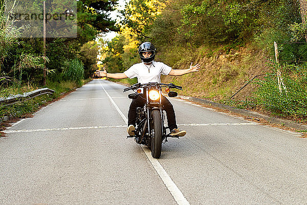 Junger Mann auf einem alten Motorrad auf einer Bergstraße bei Sonnenuntergang