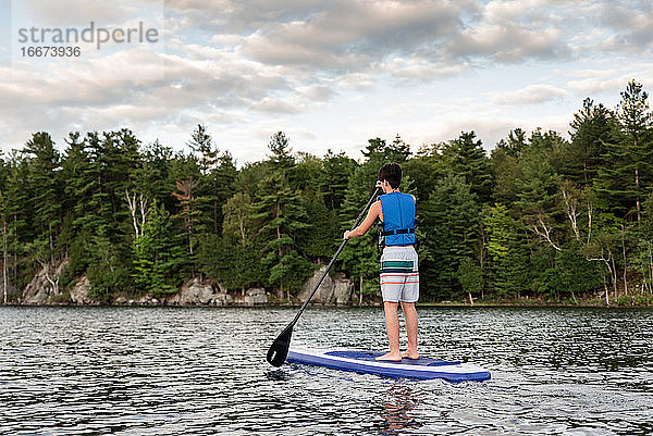Ein Jugendlicher paddelt auf einem SUP auf einem See in Ontario  Kanada  an einem sonnigen Tag.