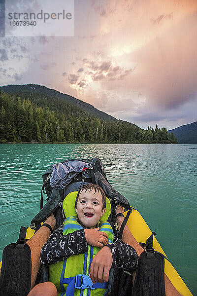 Ein kleiner Junge lächelt und lacht während einer Paddeltour mit seinem Vater.
