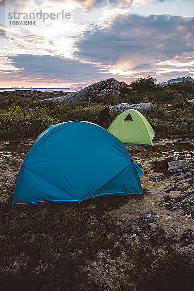 Camper öffnet Zelt bei bewölktem Sonnenuntergang