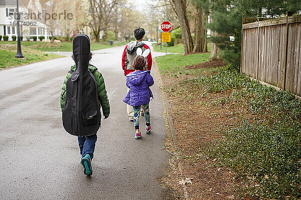 Ein Junge mit einem Cello geht mit seiner Familie eine Vorstadtstraße entlang