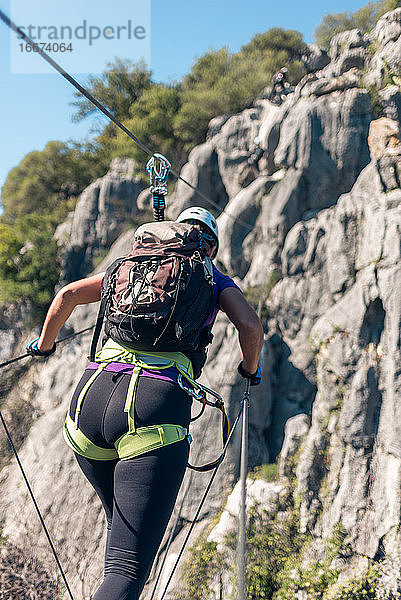 Konzept: Abenteuer. Frau mit Helm  Klettergurt und Rucksack. Gehen über den Abgrund über eine Affenbrücke. tun Klettersteig in den Bergen.