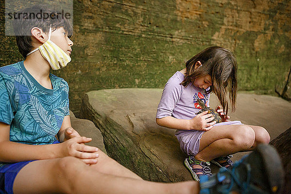 Zwei Kinder sitzen in einer felsigen Schlucht und spielen mit einer kleinen bemalten Schildkröte