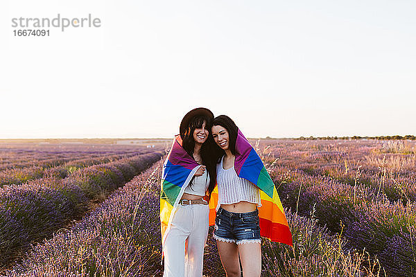 Freundinnen in einem Lavendelfeld lächelnd mit lgbt Stolz Flagge