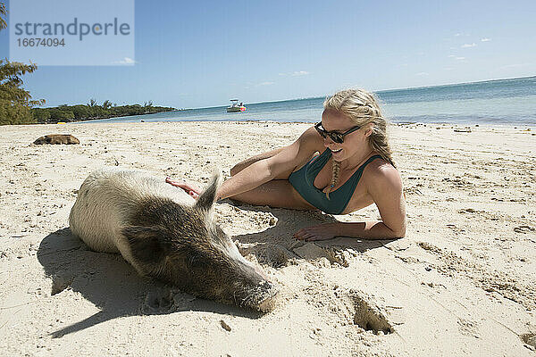 Glückliche junge Frau liegt mit einem Schwein im Sand am Strand während des Sommerurlaubs