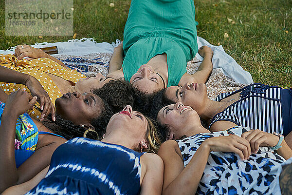 Gruppe lächelnder Freundinnen  die auf einem Handtuch in einem Park liegen