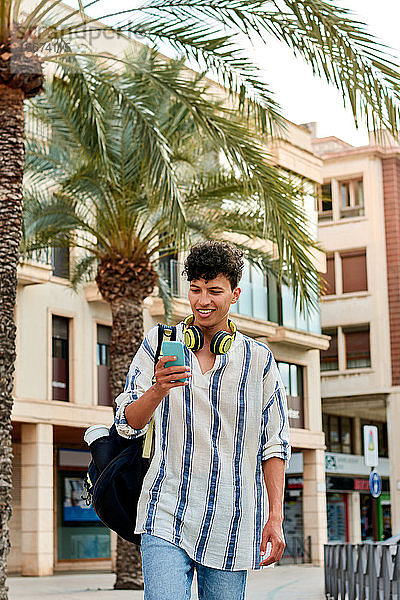 Junger afro-haariger Mann geht die Straße entlang und schaut auf sein Handy