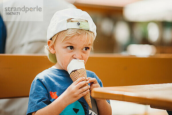 Blondes Kleinkind isst Eiswaffel sitzend auf Bärengartenbank