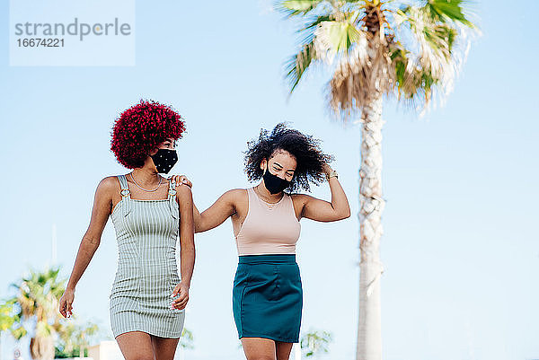 Zwei lateinamerikanische Frauen mit Schutzmaske gehen eine Promenade entlang.