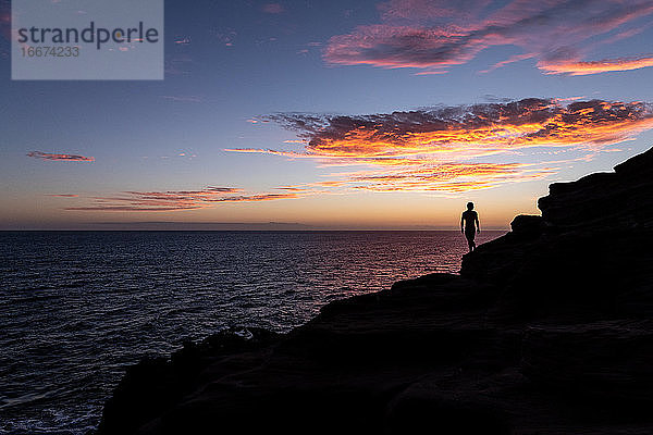 silhouette eines mannes auf einer klippe mit sonnenuntergang über dem ozean in hawaii