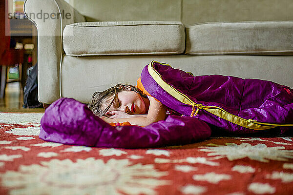 Ein hübsches kleines Mädchen liegt in einem Schlafsack auf dem Boden in einem Haus