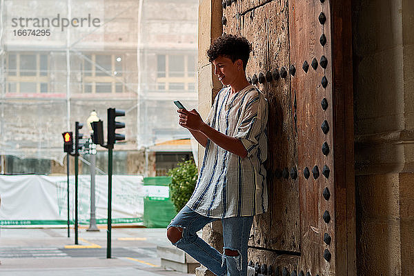Der junge Afro lehnt an einem Holztor und schaut auf sein Handy