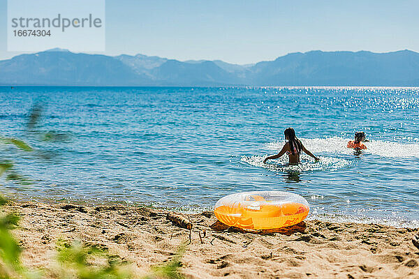 Schwimmen in einem Bergsee mit blauem Himmel und einem orangefarbenen Schlauchboot