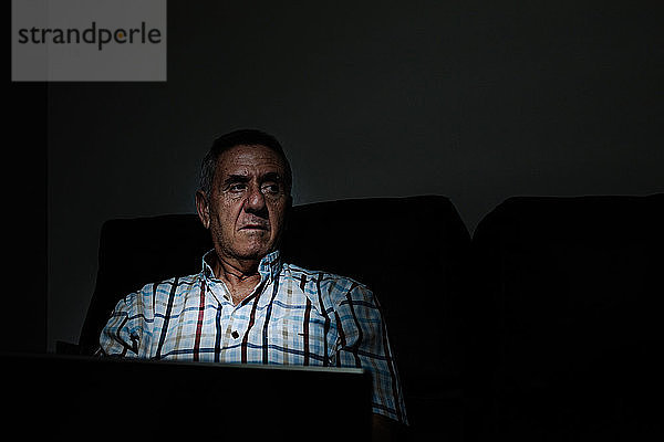 Älterer Mann beim Surfen auf dem Laptop in einem dunklen Raum
