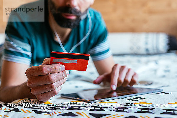 Close up Hand hält Kreditkarte und Online-Shopping auf dem Bett.