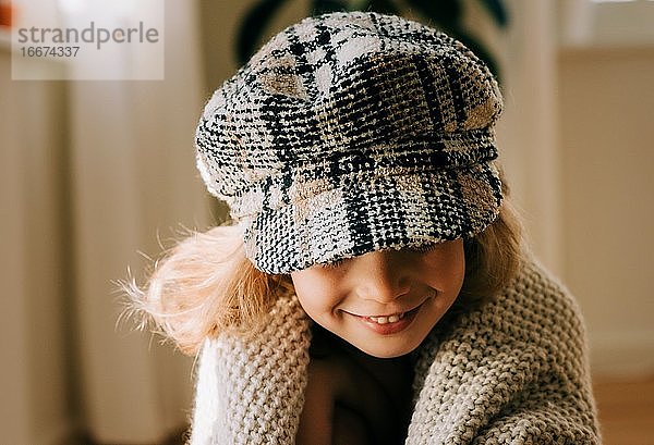 Porträt eines jungen Mädchens mit Hut  das zu Hause spielerisch lächelt