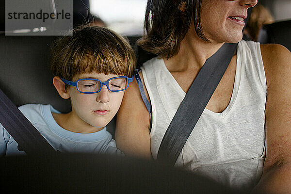 Ein kleines Kind mit blauer Brille schläft auf der Schulter der Mutter im Auto