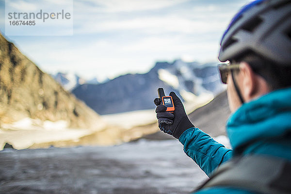 Ein Bergsteiger benutzt ein GPS  um auf einem hohen Bergpass zu navigieren.