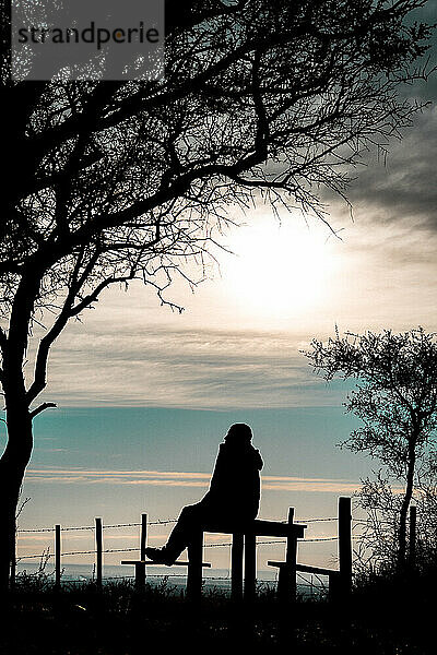 Silhouette eines Mannes  der bei Sonnenaufgang auf einer Bank sitzt