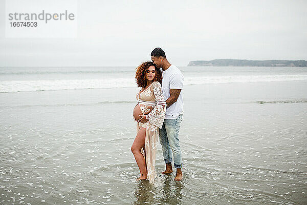 Gemischtrassiges Paar posiert am Strand  Mutterschaft