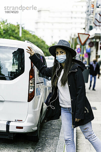 junge Frau in der Stadt  die eine Gesichtsmaske trägt und ein Taxi anhält