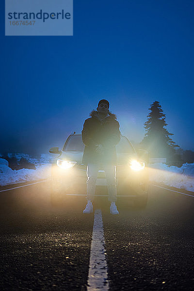 Junger Mann posiert mit seinem Auto im Hintergrund in einer verschneiten Nacht