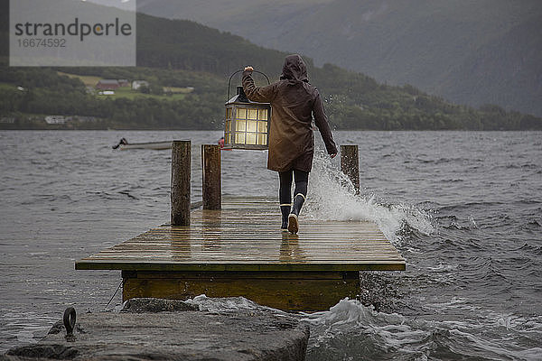 Eine Person mit einer Laterne auf einem Steg im Regen