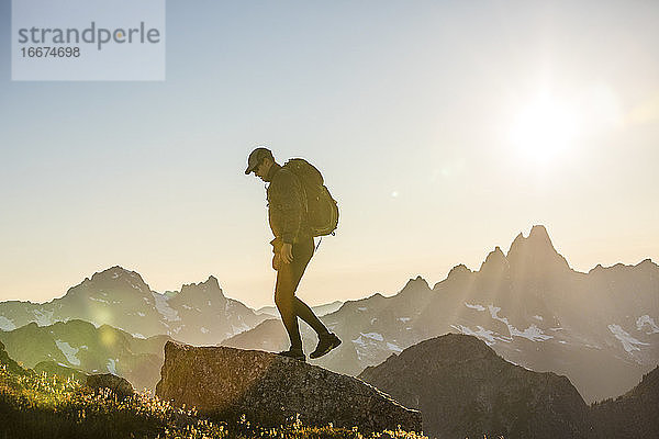 Back lit Backpacker stehend auf Berggipfel mit malerischer Aussicht