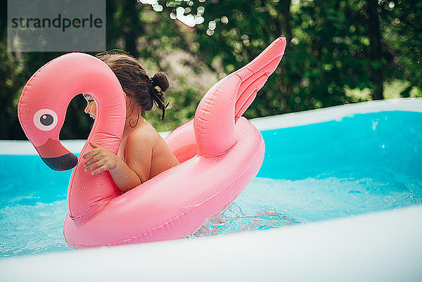 Glückliches Kind spielt im Pool mit Flamingo-Wasserspielzeug