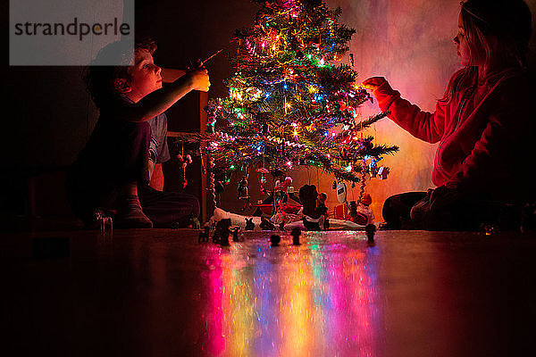 Kleine Kinder schmücken ihren Weihnachtsbaum bei Nacht