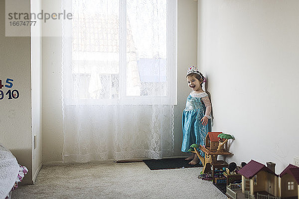 Lächelndes Mädchen im Prinzessinnenkostüm steht neben Spielzeug am Fenster