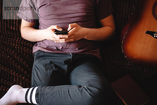 Junger Mann benutzt sein Smartphone  während er zu Hause auf dem Sofa sitzt