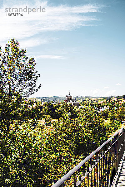 Kirche in der Mitte des Feldes  hohe Bäume  aufgenommen von einer Brücke