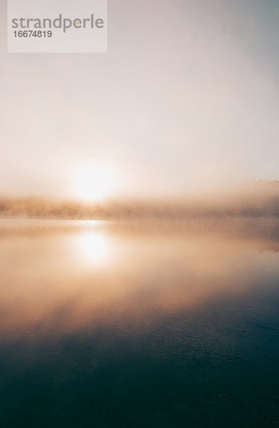 Dichter Nebel über einem ruhigen See bei Sonnenaufgang.