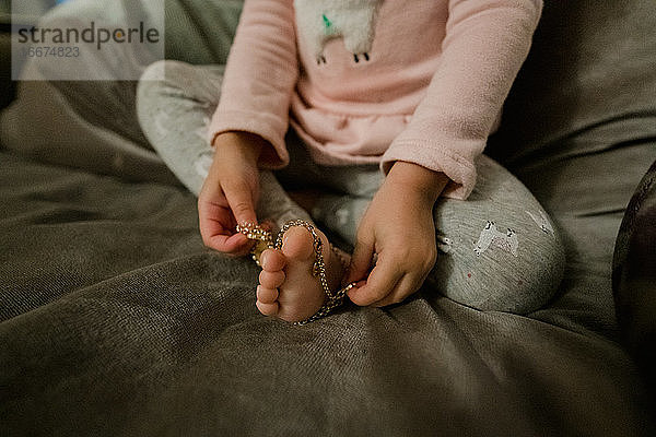 Kleinkind Mädchen spielen mit Perlen Halskette. mit ihren Füßen