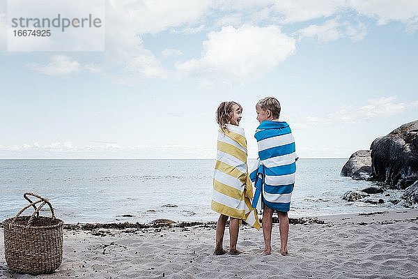 Bruder und Schwester standen lachend am Strand  in Handtücher gehüllt