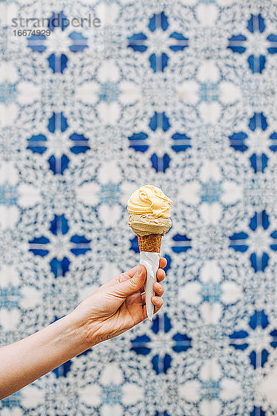 Hand hält Eiswaffel mit blauem und weißem Ornament auf dem Hintergrund