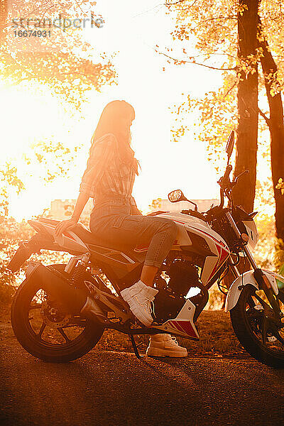 Silhouette einer auf einem Motorrad sitzenden Frau auf einer Landstraße bei Sonnenuntergang