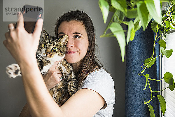 Frau zu Hause  die Selfies mit ihrer Katze am Fenster macht