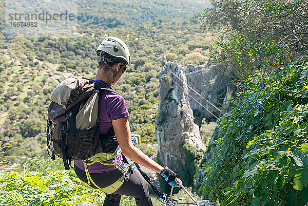 Abenteuer. Frau mit Helm  Klettergurt und Rucksack. Abstieg in den Bergen über einen Klettersteig.