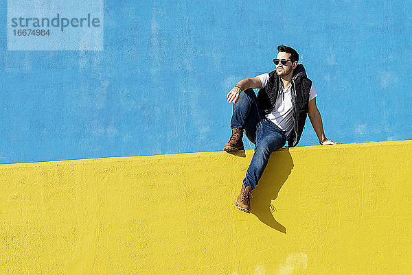 Bärtiger Mann in weißem T-Shirt  Jacke und Jeans vor blauem Hintergrund