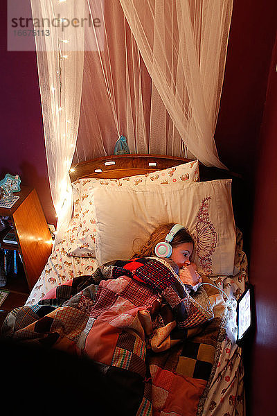 Ein junges Mädchen lernt vor einem Tablet  während es im Bett liegt